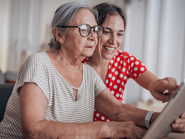 An elderly woman sitting next to her daughter looking at an ipad screen ?? 